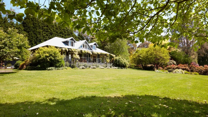 Exterior view of a country house with a manicured green lawn and surrounding trees framed by overhead branches in Sydney