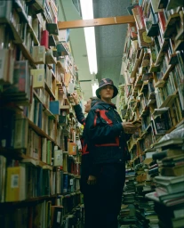 Two people browsing inside a narrow bookstore aisle packed with tall wooden shelves overflowing with books in Melbourne