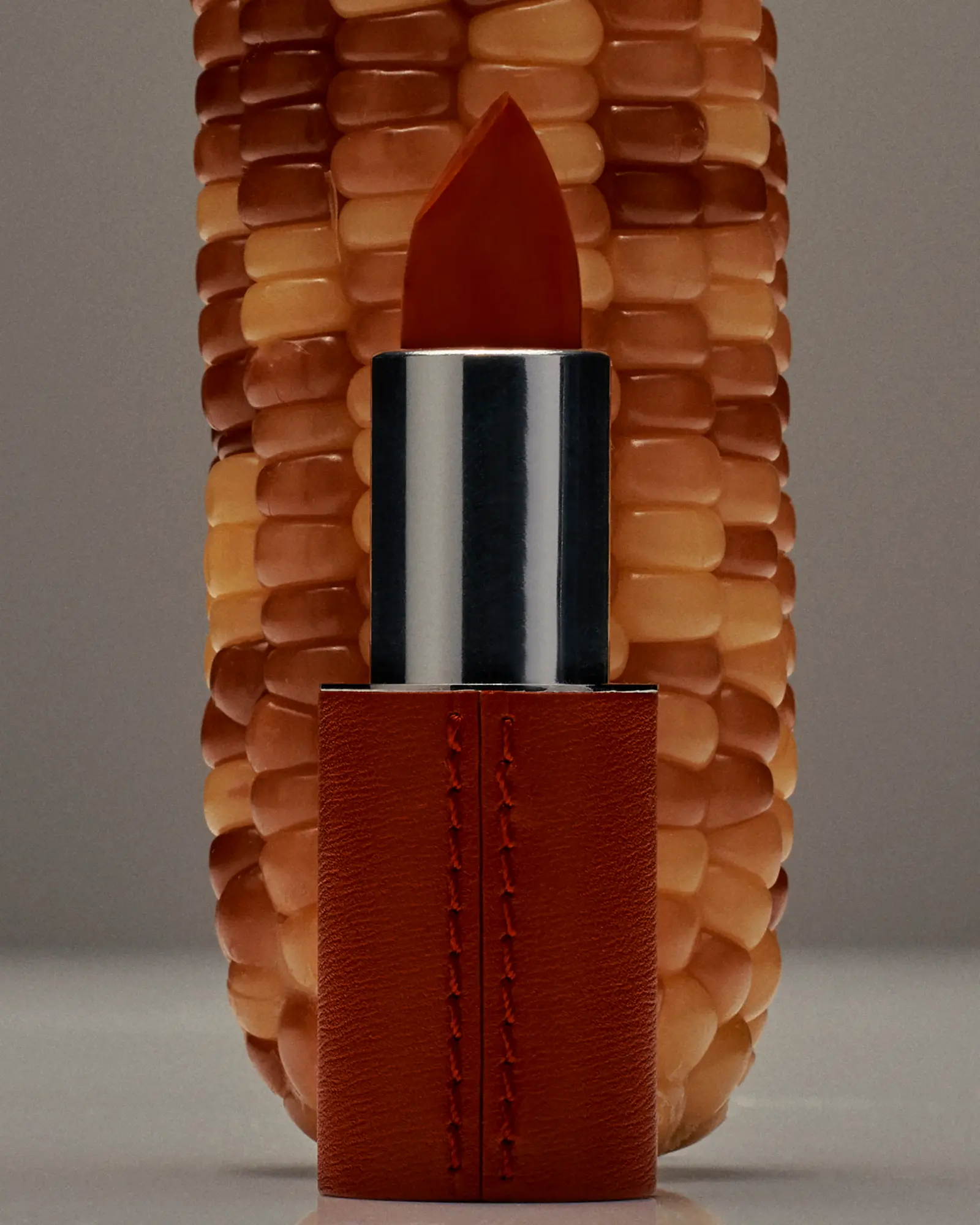 A lipstick is placed in front of a corn cob, creating a beauty advertisement, with a unique and creative presentation in a studio setting.