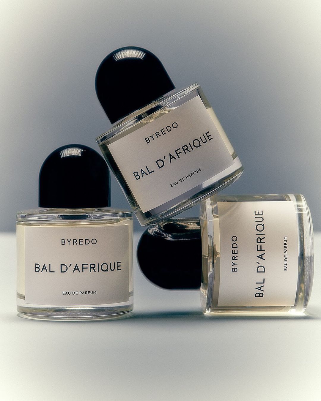 Three clear glass Byredo Bal d'Afrique perfume bottles with black caps arranged on a white surface against a soft grey background.