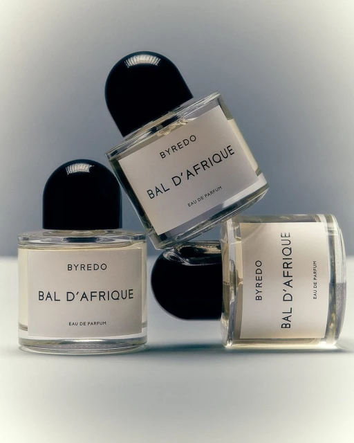 Three clear glass Byredo Bal d'Afrique perfume bottles with black caps arranged on a white surface against a soft grey background.