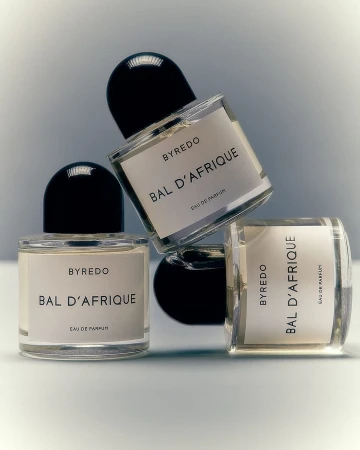 Three clear glass Byredo Bal d'Afrique perfume bottles with black caps arranged on a white surface against a soft grey background.