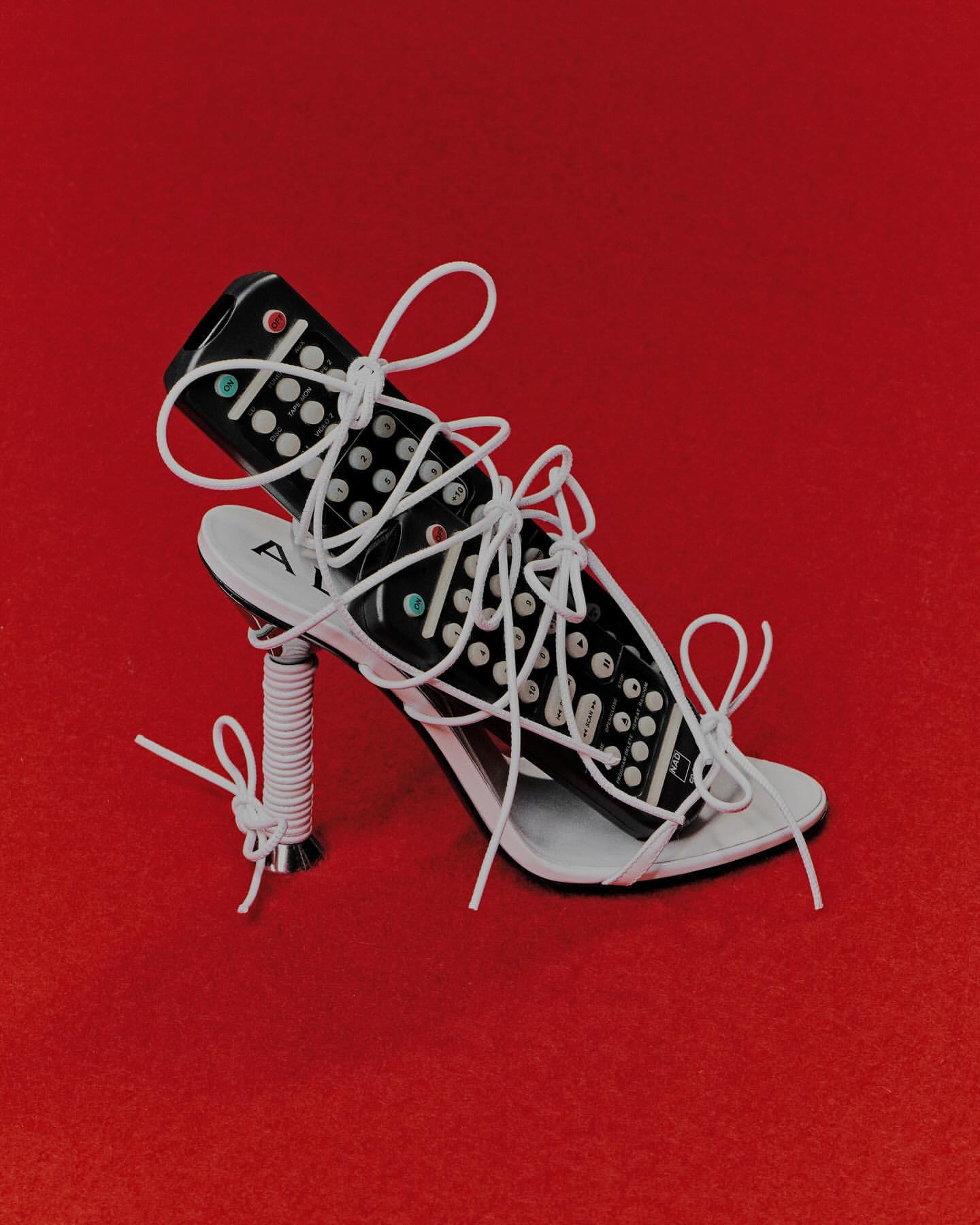 Modern art: High-heeled shoe and television remote are tied together with white string on a red background in studio lighting.