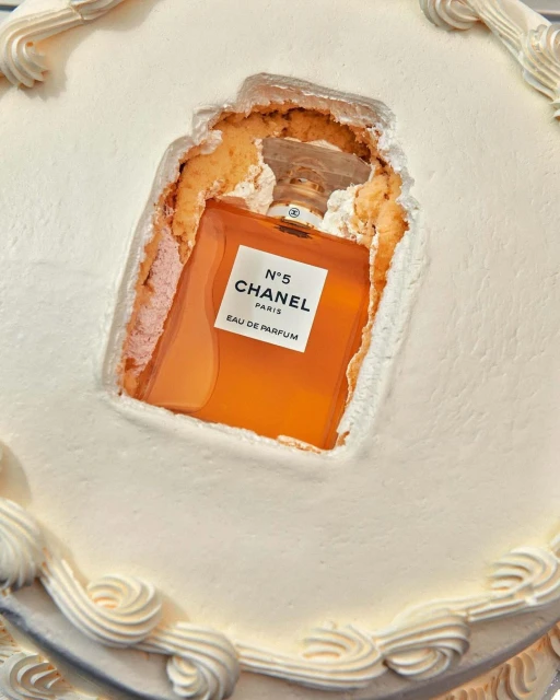 Elevated view of a square white cake with decorative frosting, featuring a Chanel No. 5 perfume bottle inside a carved-out section.