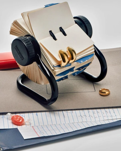 Rotary card file with blank cards and gold-colored metal clips, organized on a desk with papers and a wrapped candy.