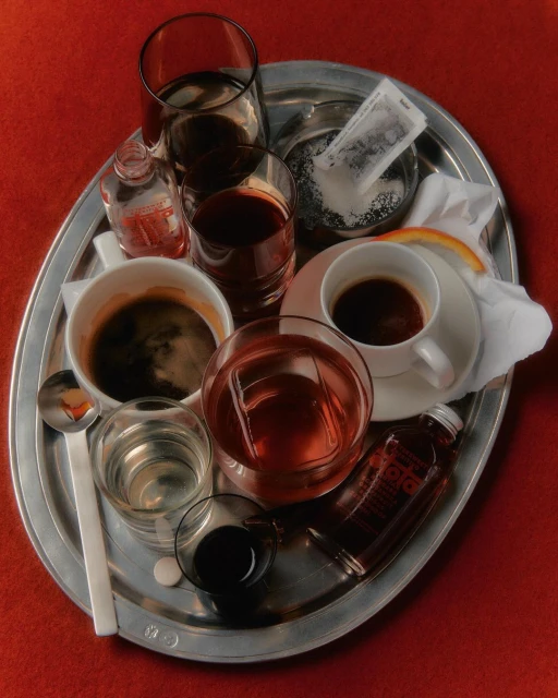 Elevated shot of a silver tray holding an assortment of beverages in glasses and cups, including coffee, water, and mixed drinks.