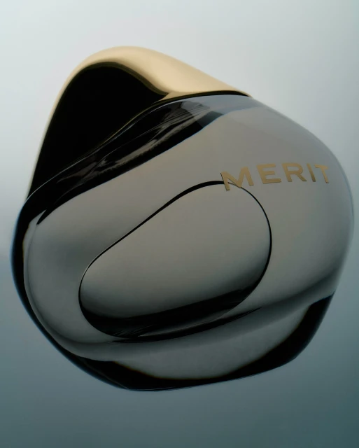 Elegant product shot of a glossy, dark gray 'MERIT' branded container with a shiny gold lid, set against a soft gradient background.