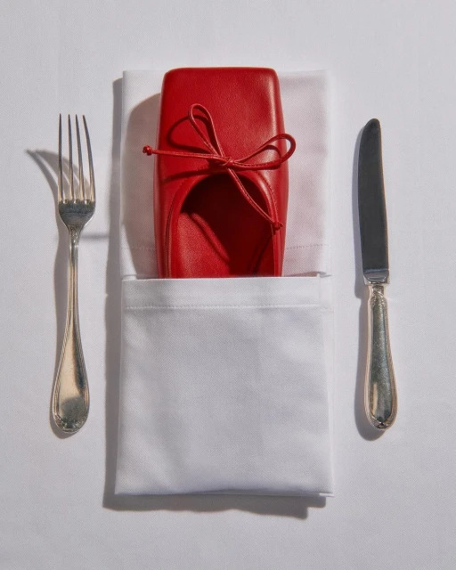 Overhead studio shot showcases a bright red shoe presented as a place setting, complete with silverware and a white napkin.