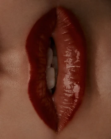 Close-up macro photography of glossy red lips parted slightly to reveal white teeth, captured by Lauren Bamford.