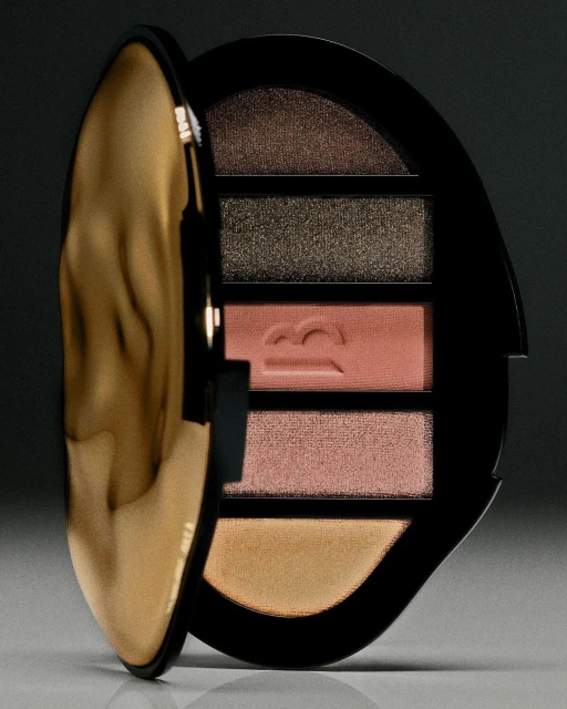 Close-up of an open makeup palette with five different eyeshadow colors and a shiny gold lid against a dark background.