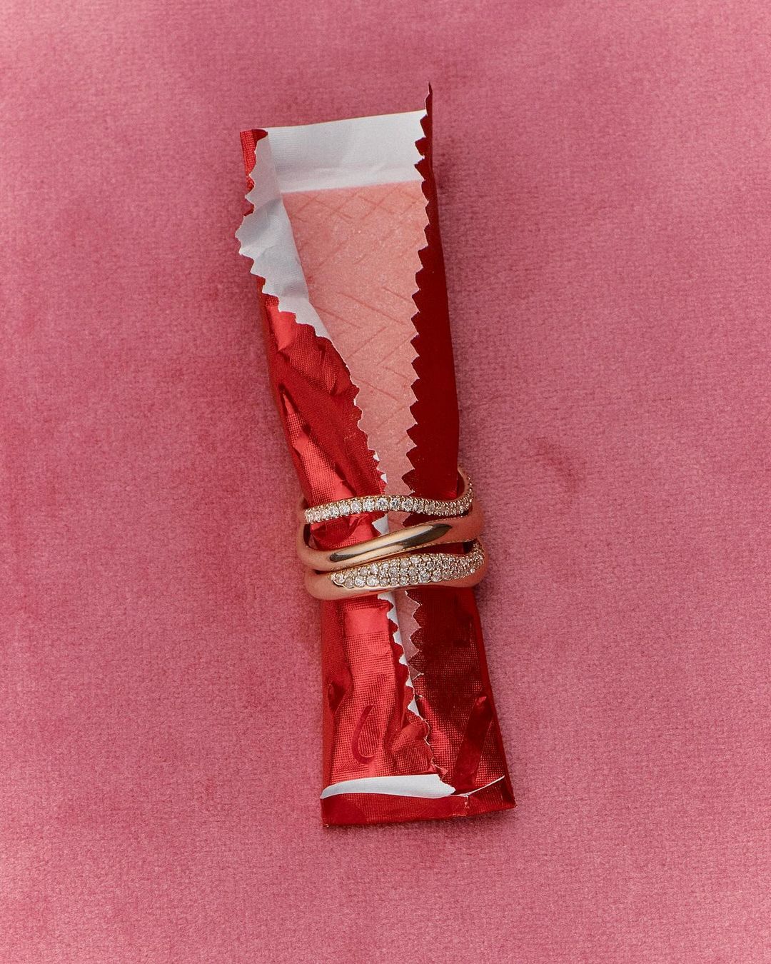 Close-up of rings stacked on a gum wrapper against a pink velvet backdrop, ideal for showcasing jewelry design and product photography.