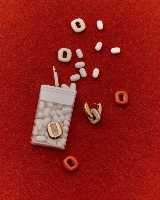 Still life flat lay: earrings, mints, and colorful shapes are arranged on a red, textured surface, creating a visually appealing composition.