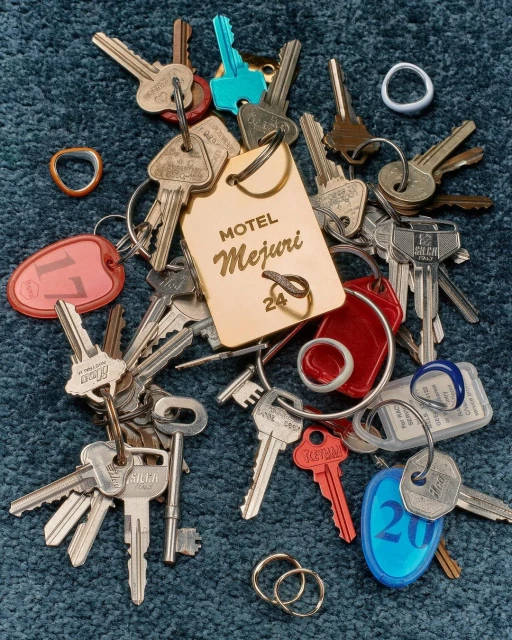 Close-up of an assortment of keys with various designs, colors, and keychains scattered on a textured blue surface.