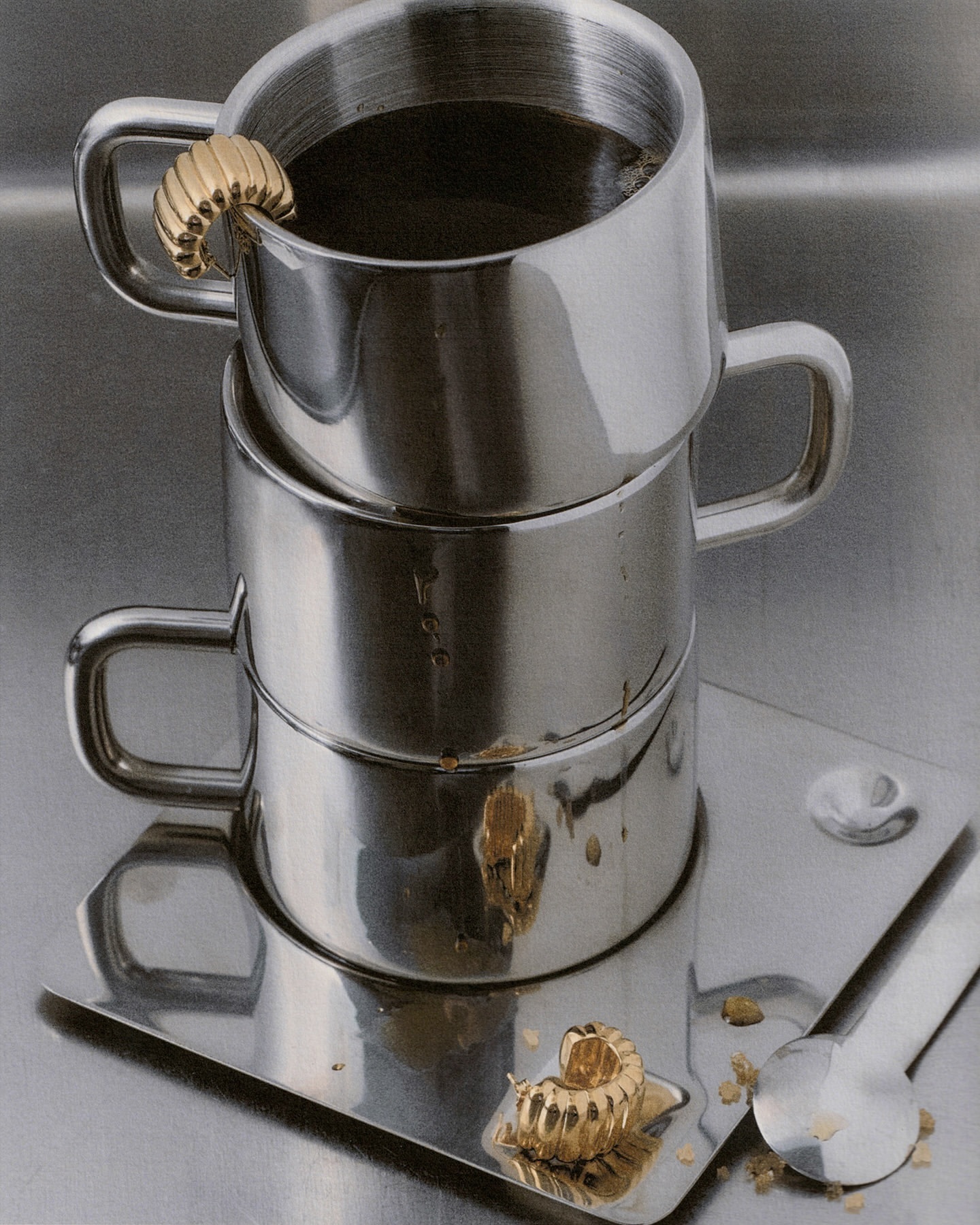 Stacked shiny metal coffee mugs with golden decorative elements, set on a metal tray with spilled coffee and scattered sugar.