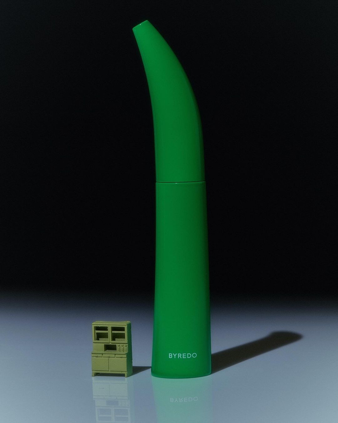Green Byredo fragrance bottle and miniature green cabinet against dark backdrop in product shot. Product photography. Cosmetics.