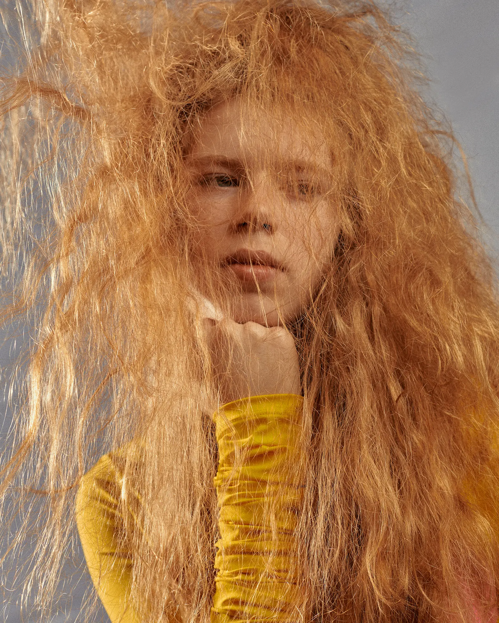Young woman with red hair and a yellow top poses indoors. The close-up shot captures a modern fashion style with a neutral background.