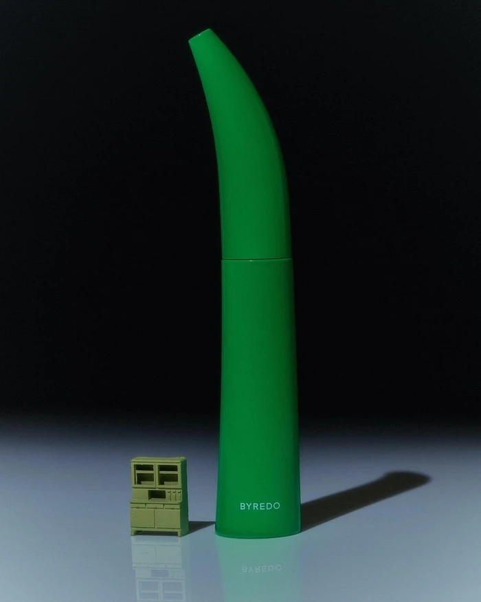 Bright green elongated tube beside a tiny miniature olive green cabinet on a dark gradient background.