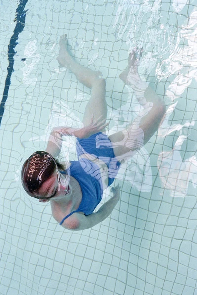 Overhead view of a woman in a blue swimsuit floating in a swimming pool with light blue tile, creating a refreshing and serene scene.