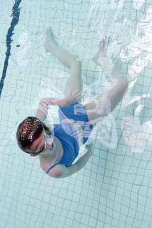 Overhead view of a woman in a blue swimsuit floating in a swimming pool with light blue tile, creating a refreshing and serene scene.