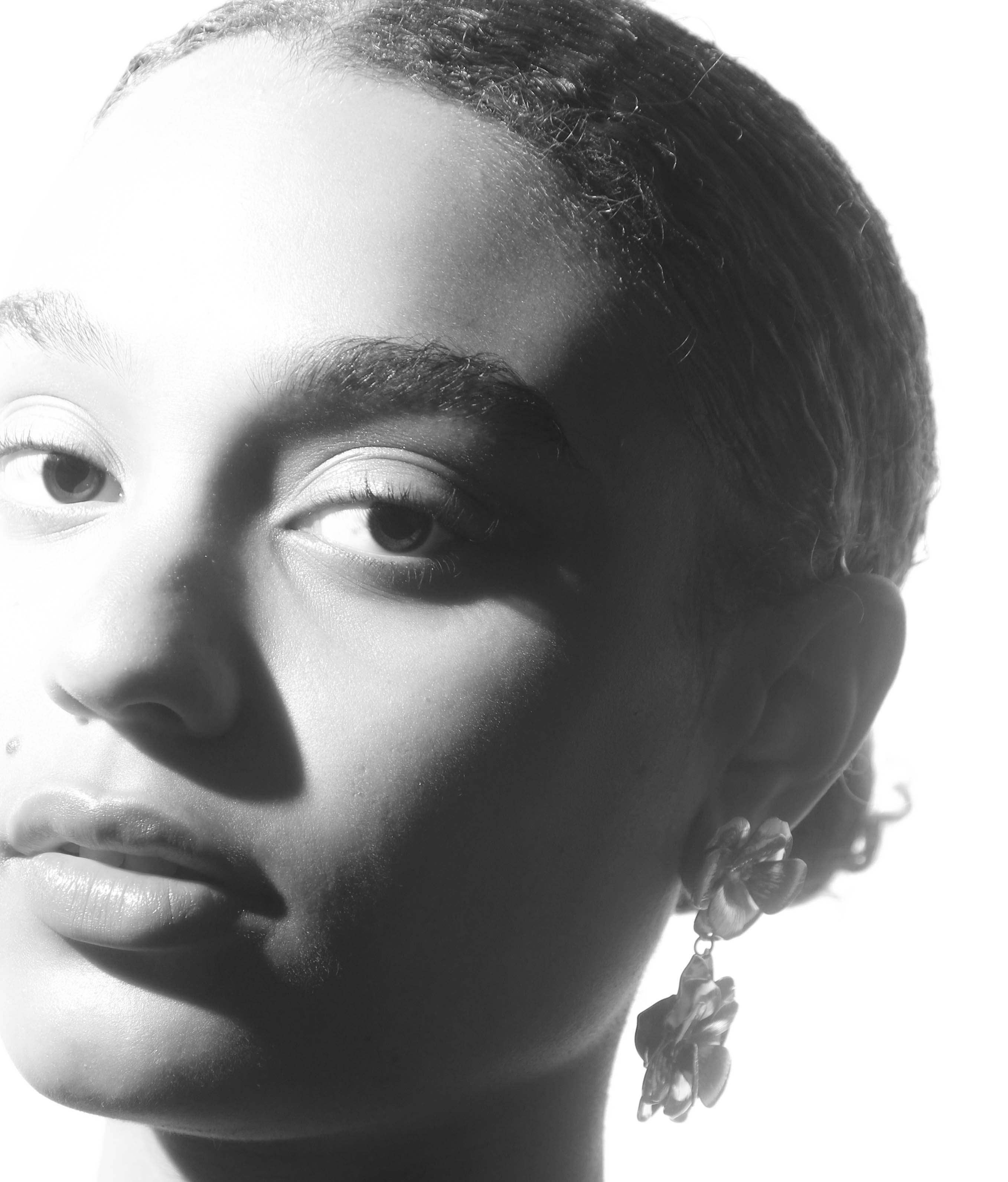 Close-up black and white portrait of a woman with floral earrings against a bright white background, showcasing beauty and fashion.