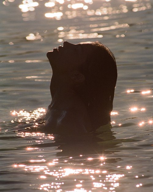 Silhouette of a dark-haired adult in water, looking upward, bathed in the warm glow of sunlit water, creating a sense of tranquility.