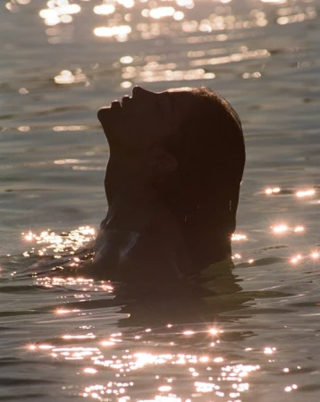 Profile silhouette of a woman swimming in water with sparkling sunlight reflections on the surface, captured by Brydie Mack.