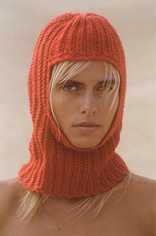 Portrait of an adult female wearing a knit balaclava in a neutral outdoor setting, emphasizing beauty and fashion elements.