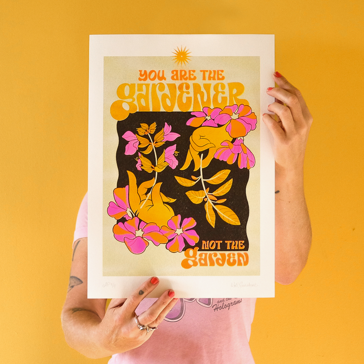 Person holds art print with text 'You are the gardener not the garden' against yellow background, featuring floral and hand illustrations.