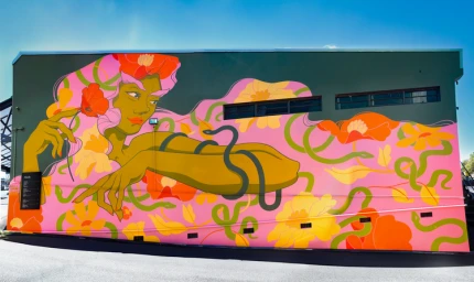 Large colorful mural on a building exterior featuring an illustrated green woman holding a red flower surrounded by pink, orange, and yellow flowers.