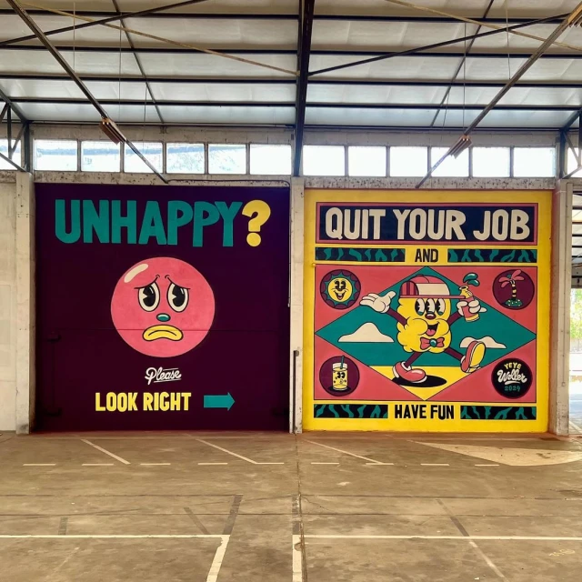 Eye-level shot of two colorful cartoon murals on warehouse doors, one with a sad face and one promoting a happy message.