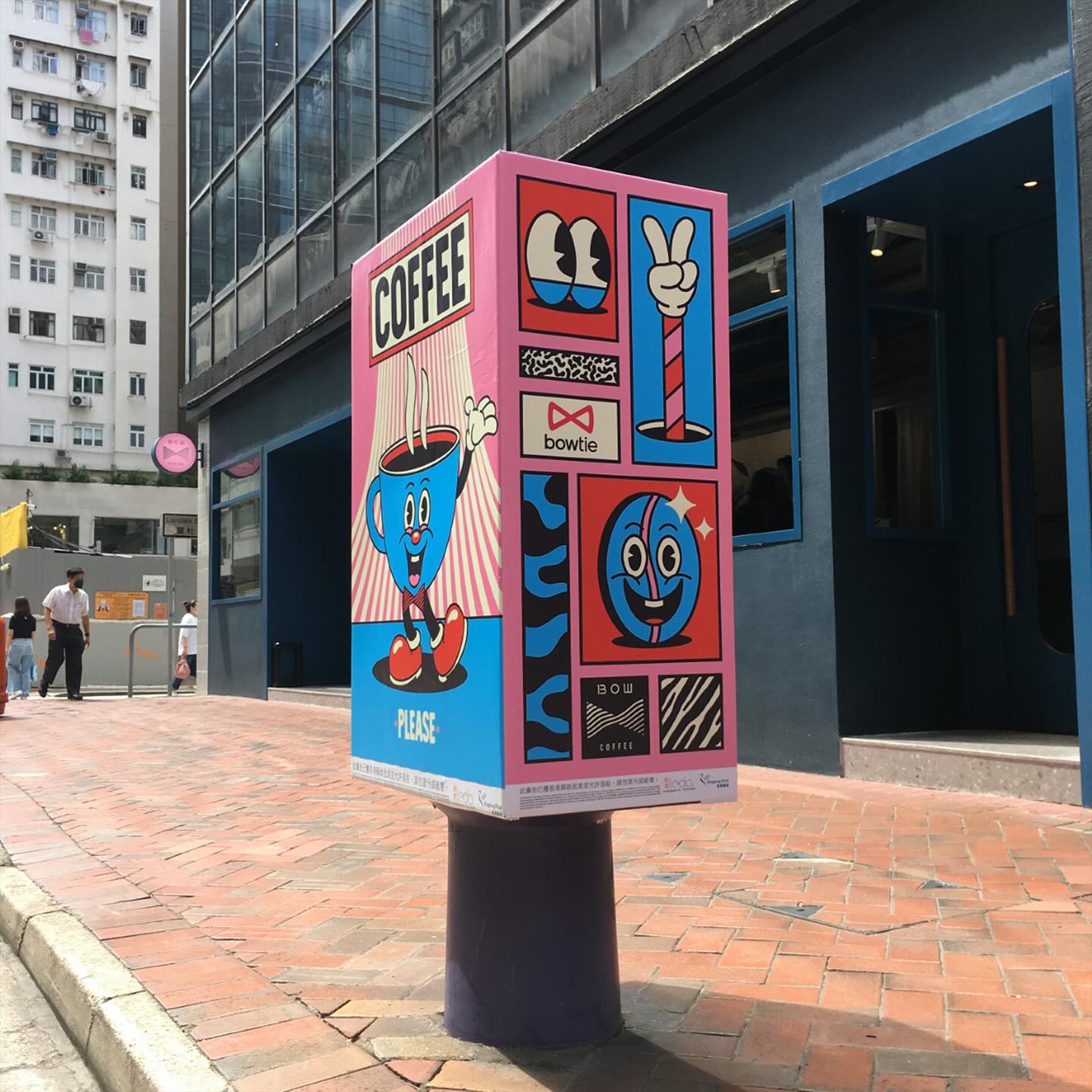 Street-side ad displays a cartoon coffee cup character and text for a coffee shop in a colorful, urban outdoor setting.