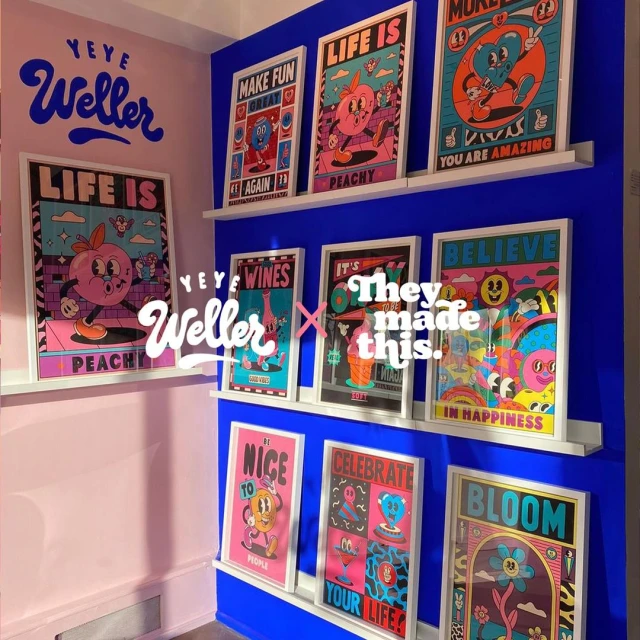 Eye-level shot of an art exhibit featuring colorful framed posters on a blue wall in a pink-walled room, showcasing various cartoon-style illustrations.