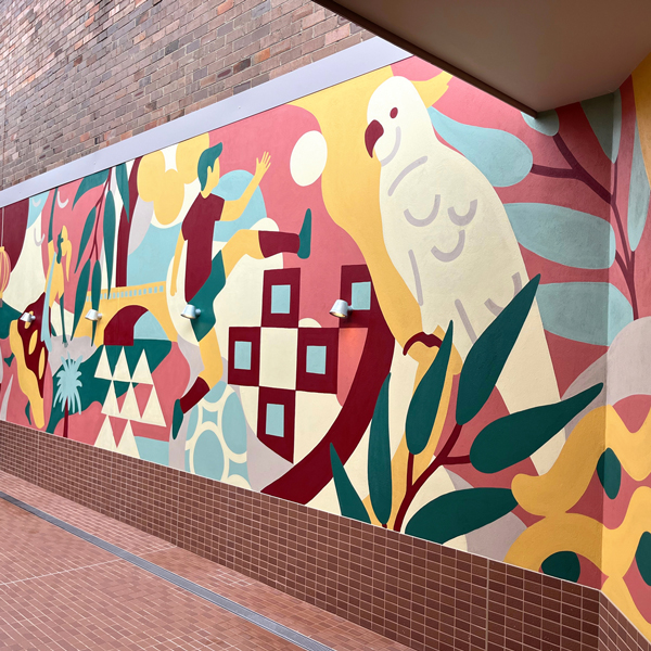 Colorful outdoor mural featuring a soccer player, abstract shapes, geometric patterns, tropical leaves, and a stylized parrot.