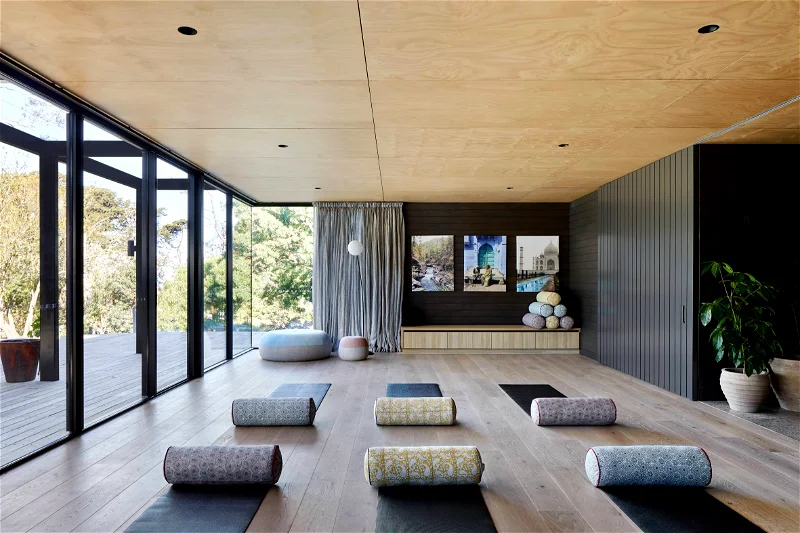 Bright indoor yoga studio featuring mats and bolsters, floor-to-ceiling windows, and natural light enhancing the serene space.