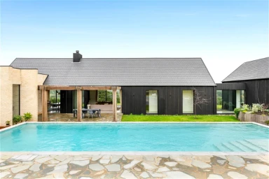 Modern dark timber house with a swimming pool and stone patio under a clear sky