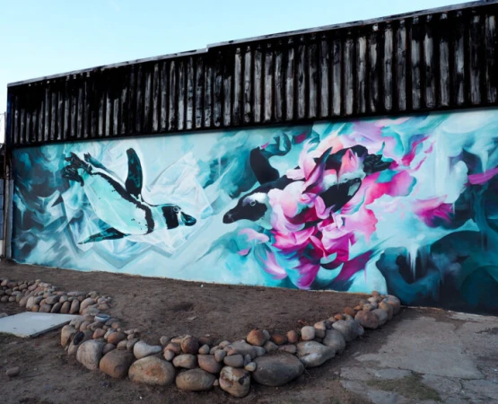 Mural art featuring penguin paintings against a light blue backdrop with stone accents, creating a vibrant outdoor setting.