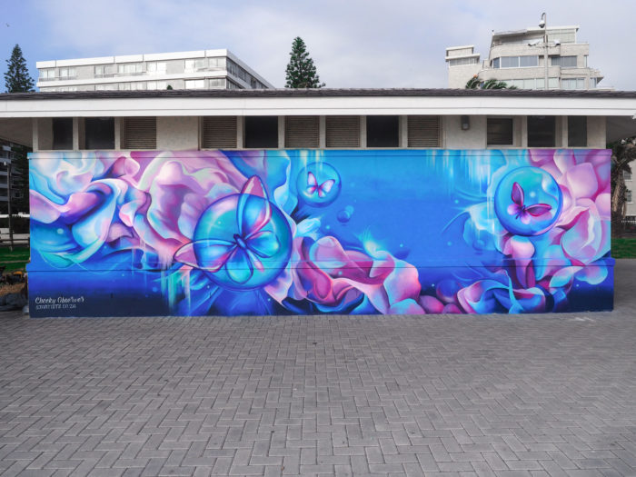 Mural featuring blue butterflies and pink floral designs on a building wall, creating a dreamy and artistic outdoor public art display.