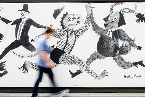 Illustration of a person blurred in motion passing a mural with stylized figures of a man, reptile, and goat on a white wall.