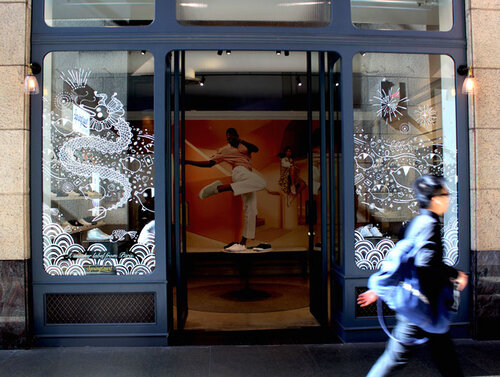 Exterior view of a retail store with a window display featuring shoes, graphic art, and a fashion image of a man in white clothing.