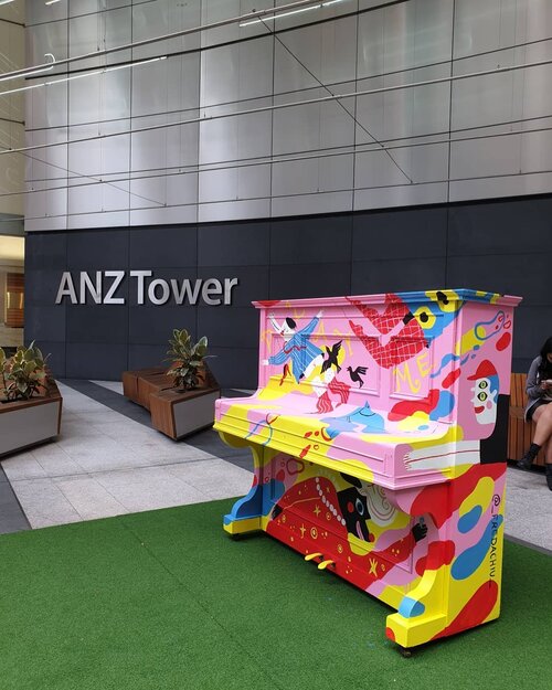 Outdoor shot of a colorful piano with vibrant paintings, set in a public space next to the ANZ Tower building, enhancing the urban environment.