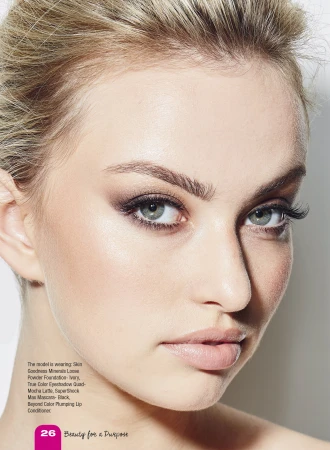 Close-up portrait of a young adult woman with light skin and blonde hair, wearing eye makeup and light pink lipstick in a beauty shot.