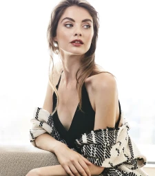 Portrait of a woman wearing a black top and patterned wrap, looking away against a bright neutral background