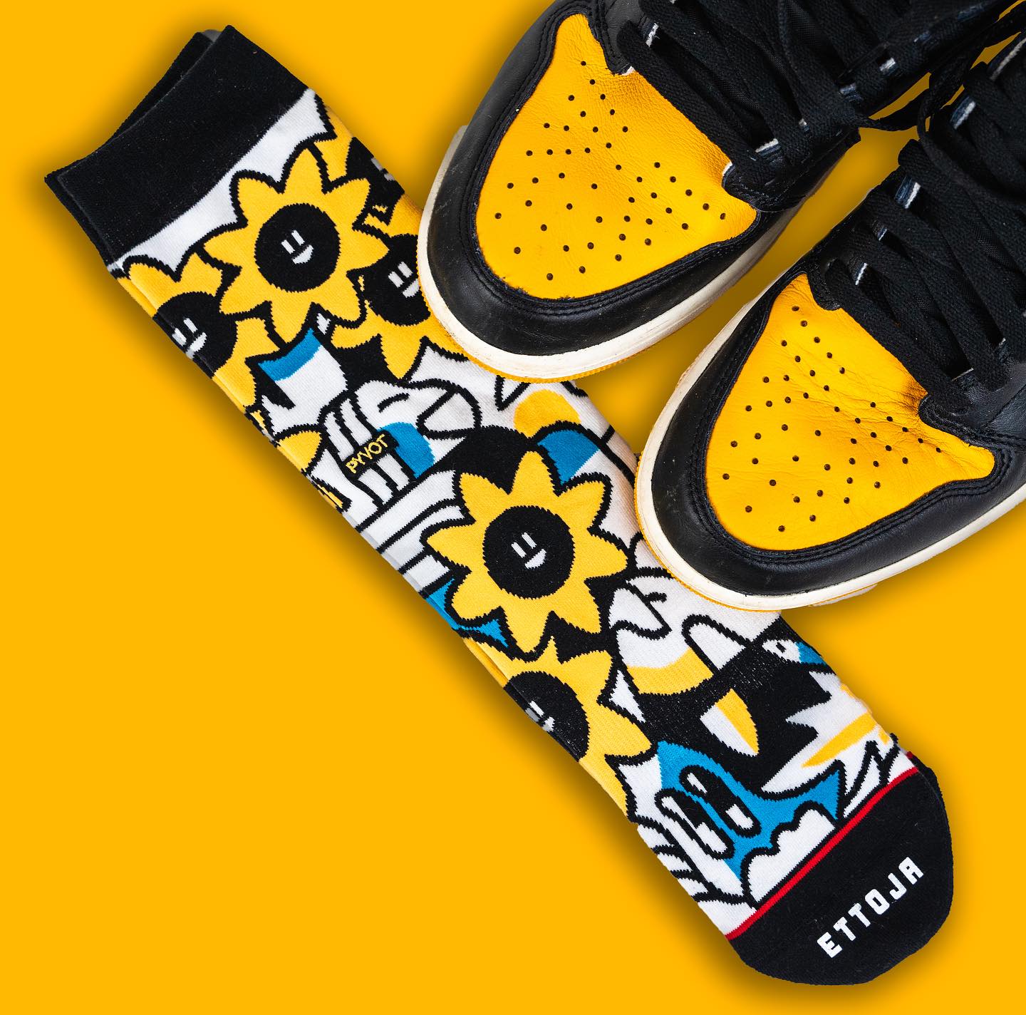 Eye-level shot showcasing an Ettoja brand sock adorned with a sunflower pattern, presented alongside a pair of black and yellow sneakers.