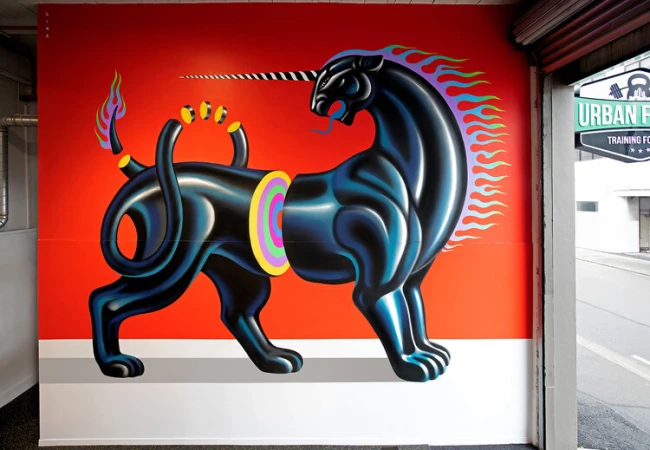 Mural of a black panther with a unicorn horn on a bright red wall, a creative combination of animals in a street art style.