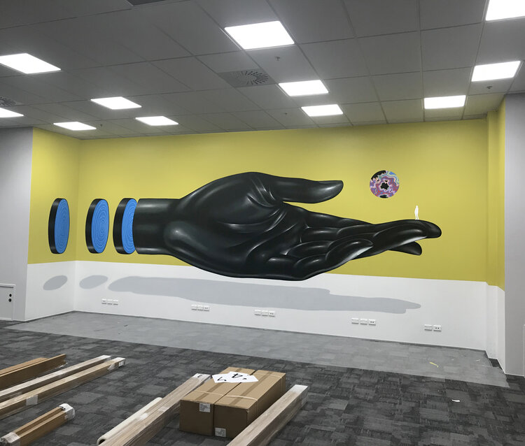 Illustration of a large black hand on a yellow wall in an indoor space, with blue and black discs and a circular graphic above the hand.