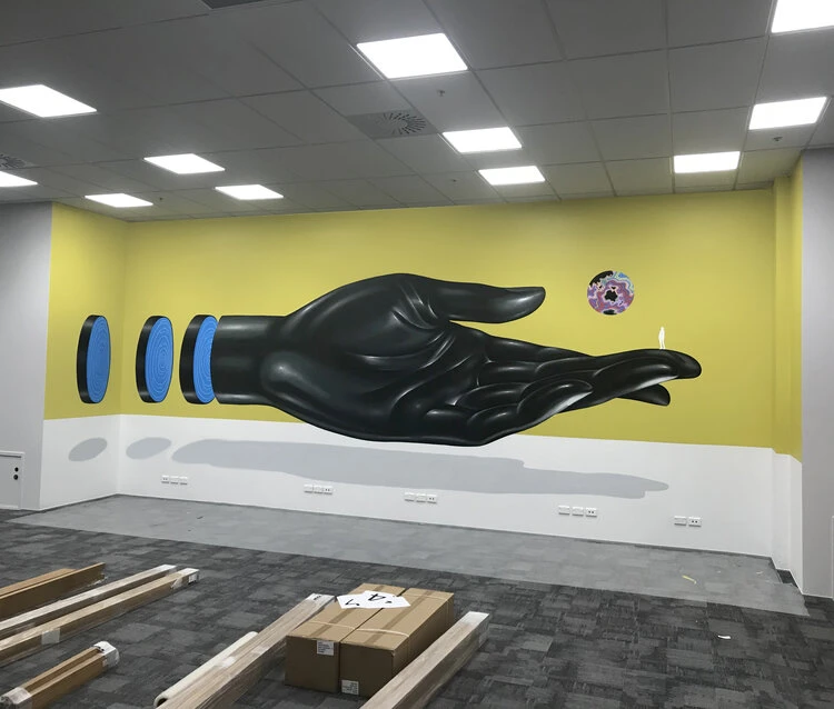 Illustration of a large black hand on a yellow wall in an indoor space, with blue and black discs and a circular graphic above the hand.