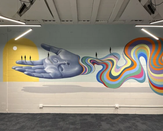 Art wall featuring a large hand mural with tiny figures walking along a colorful, wavy path. Interior with visible lighting.