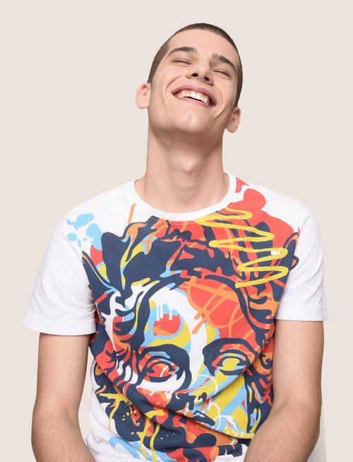 Man smiles while wearing a T-shirt with colorful graphic art. Portrait captures his joyful expression in a light studio setting.