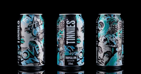 Three aluminum beverage cans featuring turquoise and black graffiti illustration work arranged against a solid black background.