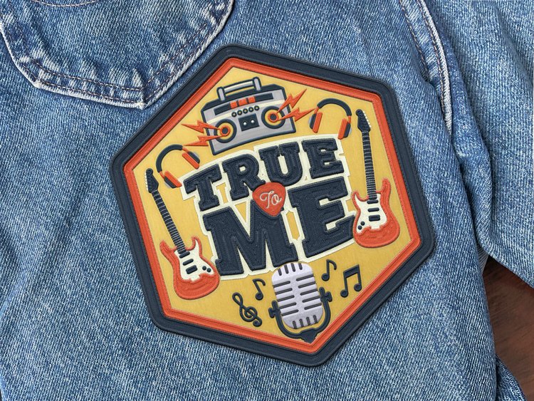 A close-up of a denim jacket featuring a vibrant music-themed patch. The patch showcases retro audio equipment and the words 'True To Me'.